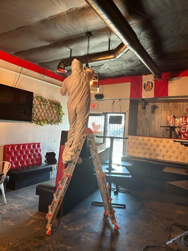 A technician on a ladder working the ceiling of a bar with red booths