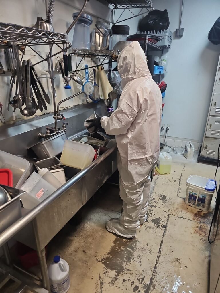 A technician working at a large sink in a commercial kitchen