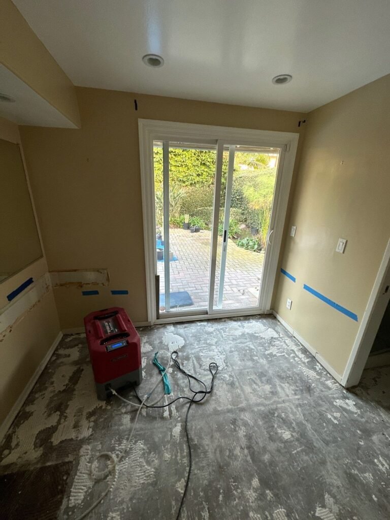 An emptied room with sliding doors to the garden and a dehumidifier on bare floor