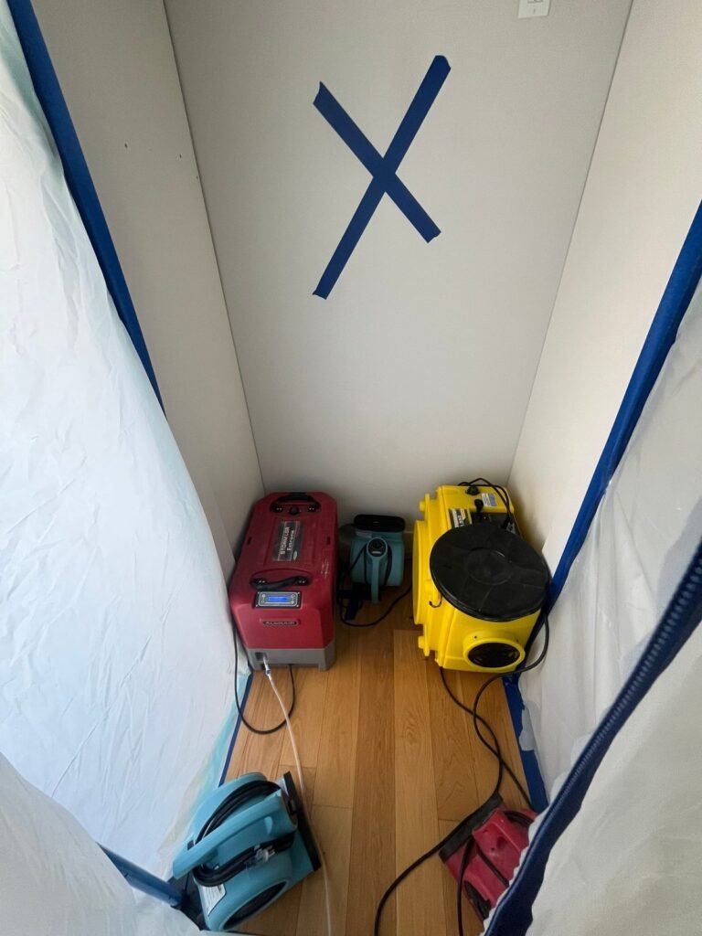 A room sealed in plastic with a blue X marking the wall and two machines running